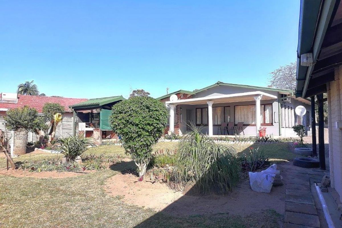 Rear view of the property featuring a covered patio area, established garden, and paved walkway.