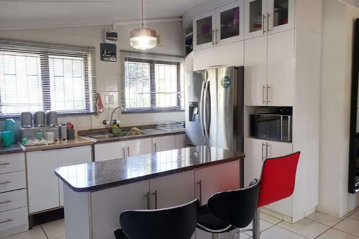 A functional kitchen featuring white cabinetry, granite countertops, tiled flooring, and a central island with integrated storage and breakfast bar seating.