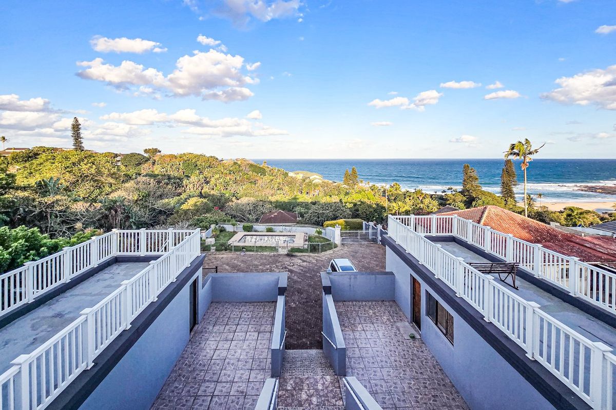 Elevated aerial view of the property featuring dual tiled patio areas, paved driveway, swimming pool, and expansive coastal ocean views.