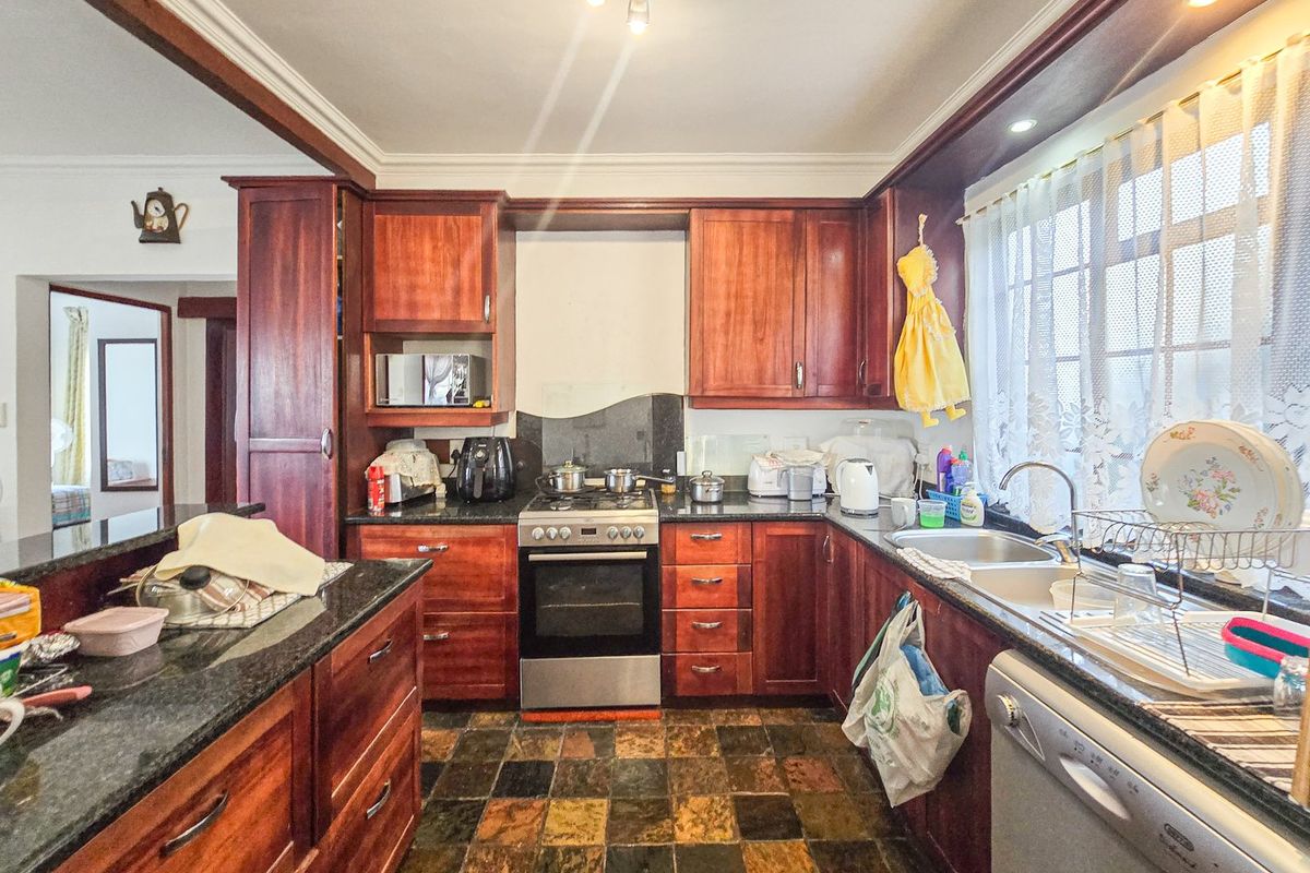 A functional kitchen featuring rich wooden cabinetry, granite countertops, a gas hob, and integrated appliances, finished with durable tiled flooring.