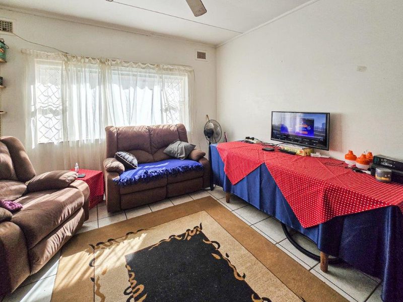A living room featuring tiled flooring, a ceiling fan, and a window with security bars, offering a functional space ready for cosmetic updates.