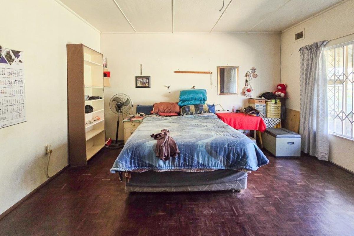 A spacious bedroom featuring parquet flooring, a ceiling fan, and a window with security bars, offering a blank canvas for renovation.