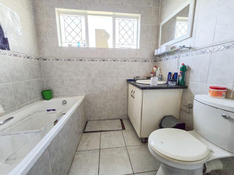 A functional bathroom featuring a built-in bathtub, vanity cabinet, and tiled finishes throughout, offering a practical layout with natural light.