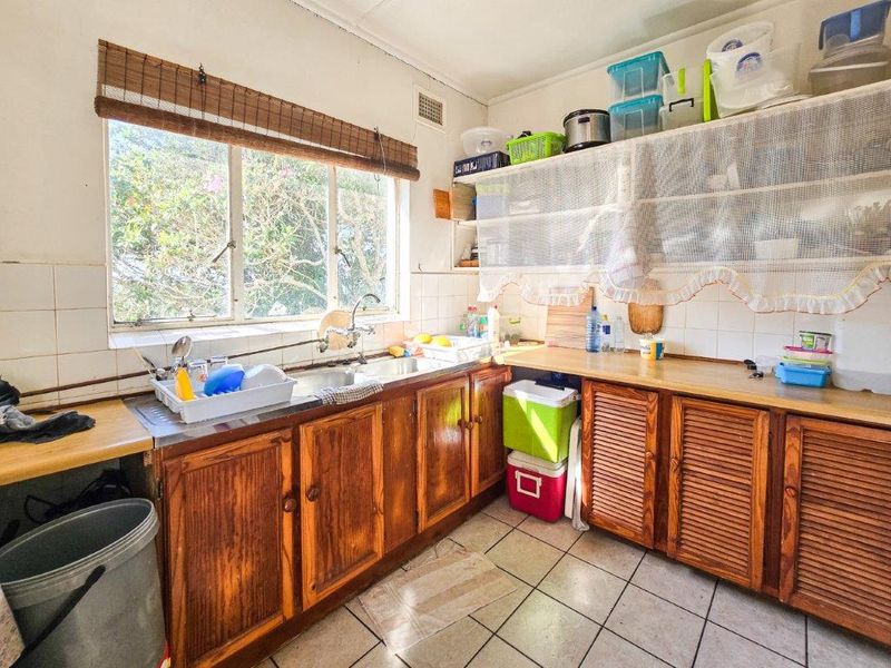 A dated kitchen featuring wooden cabinetry, laminate countertops, a double basin sink, and tiled flooring, offering potential for a modern renovation.