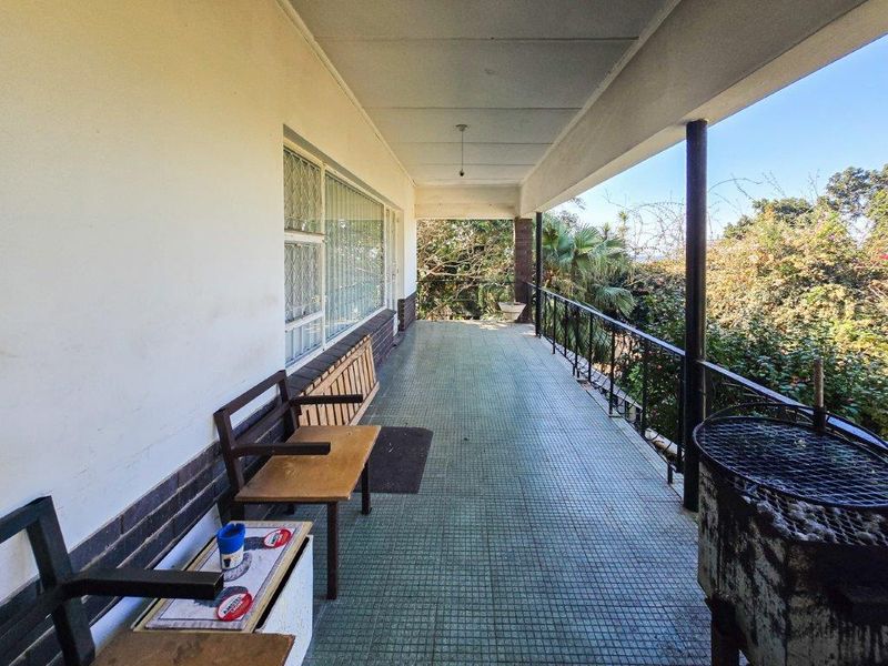 A covered outdoor patio featuring tiled flooring, metal railings, and security-barred windows, offering a functional space for outdoor relaxation.