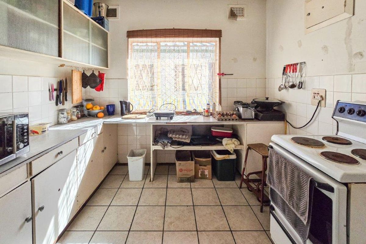 A dated kitchen featuring tiled flooring, wall-mounted cabinetry, and a freestanding electric stove, requiring cosmetic updates and modernization of finishes.