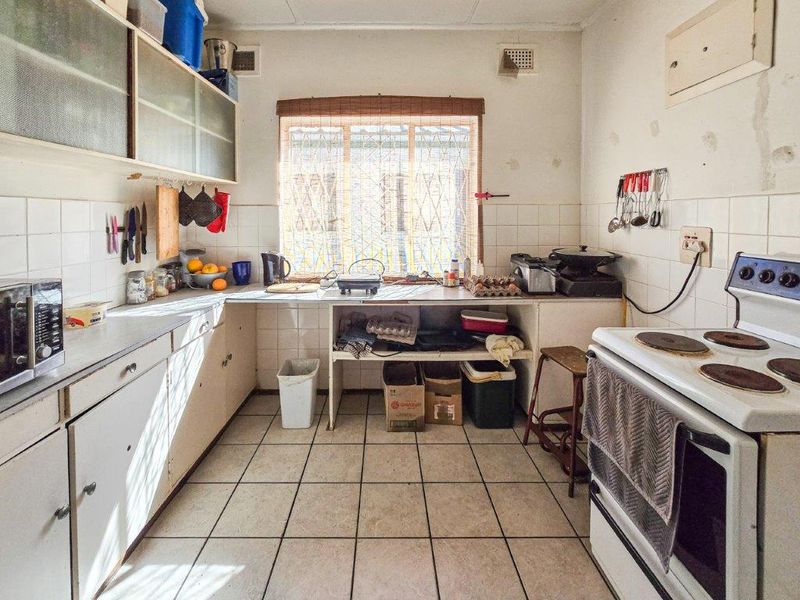 A dated kitchen featuring tiled flooring, wall-mounted cabinetry, and a freestanding electric stove, requiring cosmetic updates and modernization of finishes.