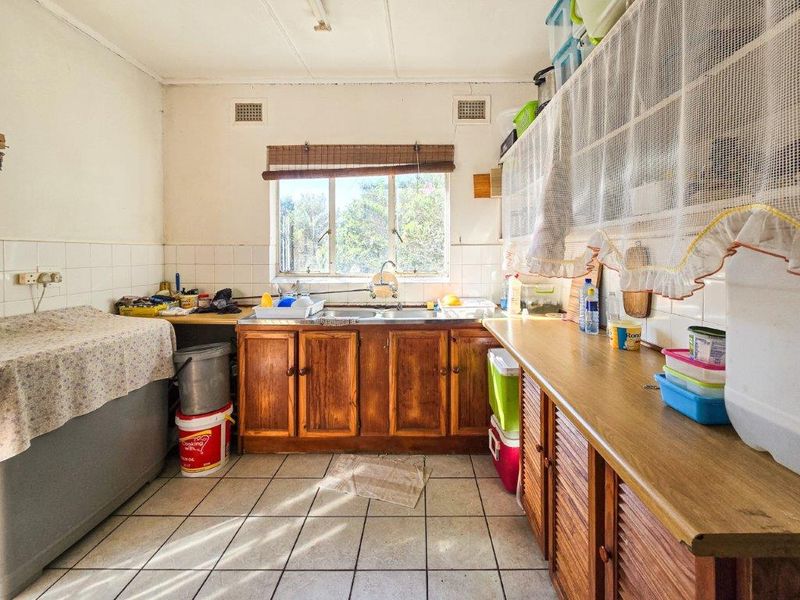 A dated kitchen featuring wooden cabinetry, laminate countertops, and tiled flooring, offering a functional layout with potential for modernization.