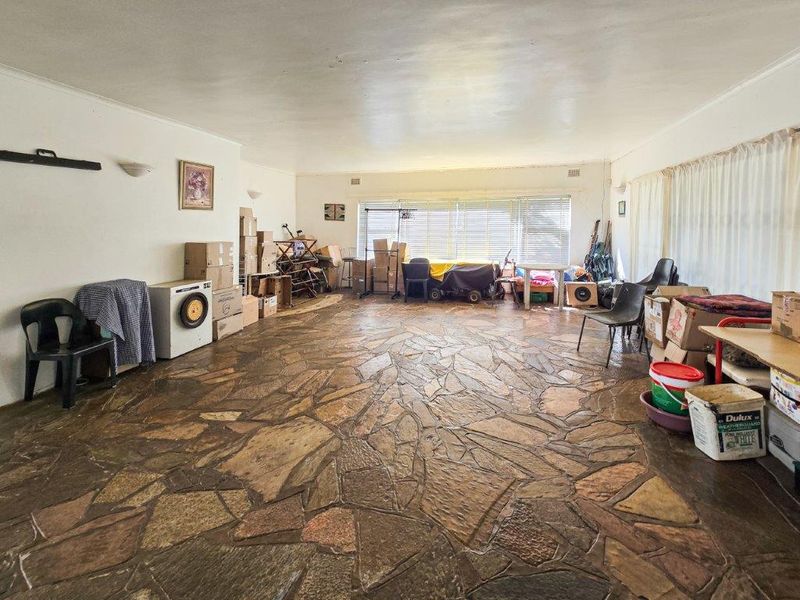 Spacious living area featuring unique flagstone flooring and large windows, offering a blank canvas for renovation and interior design updates.