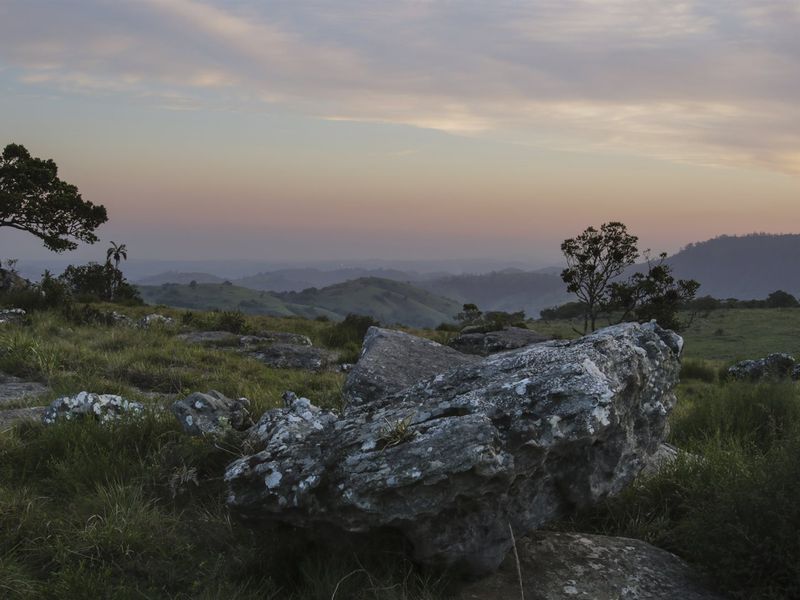 A scenic landscape view of the farm property featuring rolling hills, natural rock formations, and native vegetation at sunset.