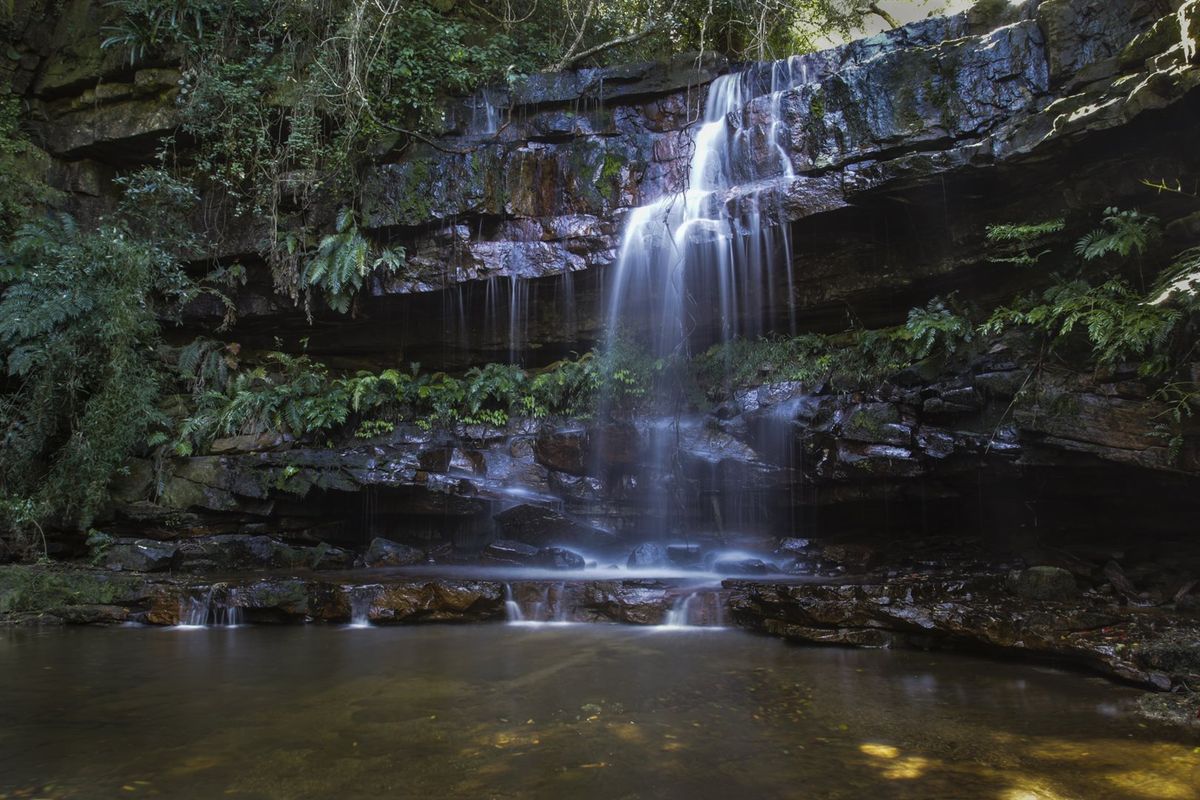 A scenic view of a natural waterfall cascading over rock formations into a tranquil pool on the property grounds.