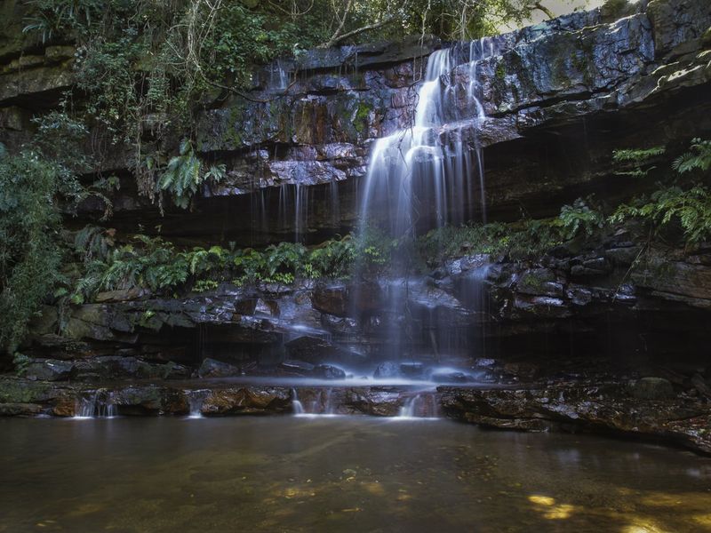 A scenic view of a natural waterfall cascading over rock formations into a tranquil pool on the property grounds.