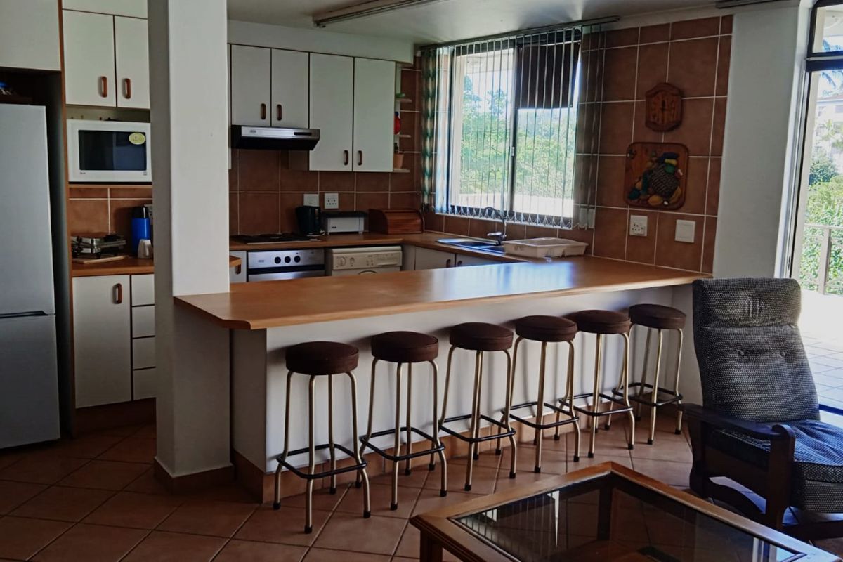 Open-plan kitchen featuring built-in cabinetry, a breakfast bar, and tiled finishes, seamlessly connecting to the living area and outdoor balcony.
