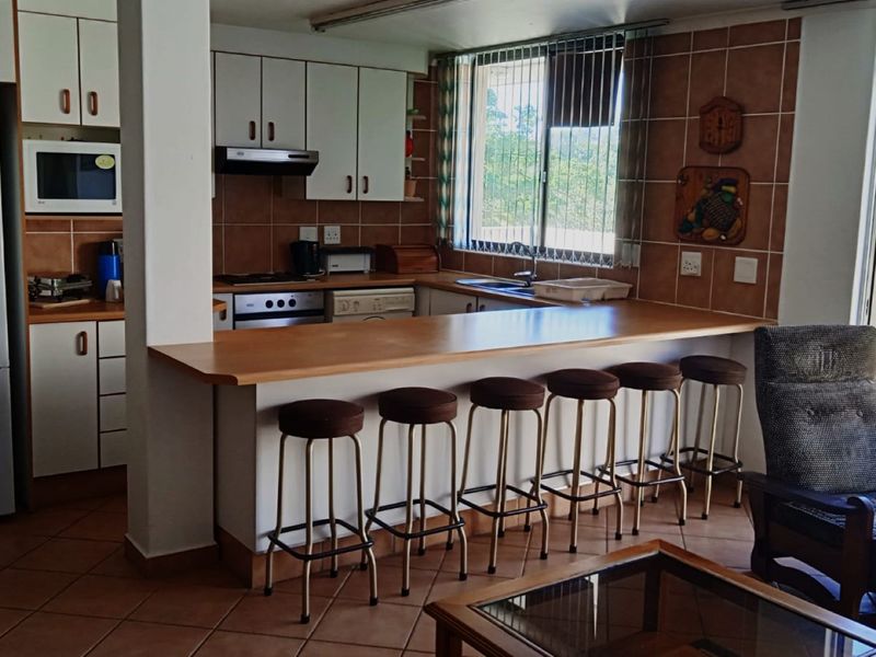Open-plan kitchen featuring built-in cabinetry, a breakfast bar, and tiled finishes, seamlessly connecting to the living area and outdoor balcony.