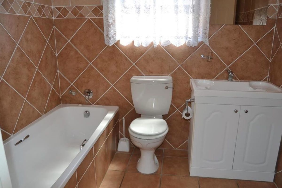 A functional bathroom featuring a bathtub, toilet, and vanity cabinet with a washbasin, finished with classic brown wall and floor tiles.