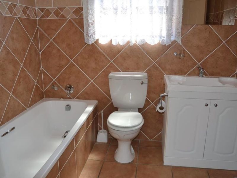 A functional bathroom featuring a bathtub, toilet, and vanity cabinet with a washbasin, finished with classic brown wall and floor tiles.
