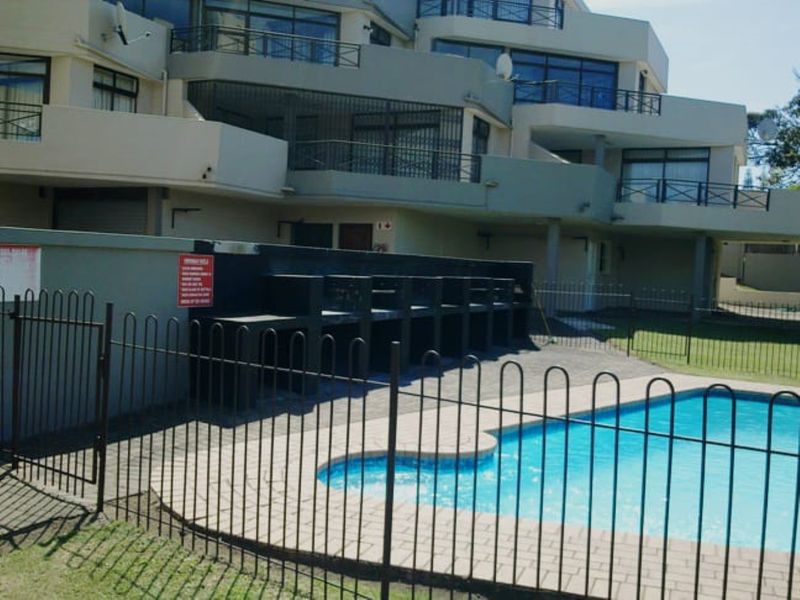 Communal swimming pool area featuring paved surrounds, metal fencing, and a built-in braai facility set against the apartment building facade.