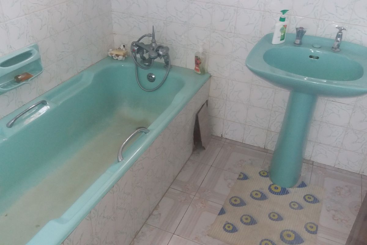 A dated bathroom featuring a vintage green pedestal basin and matching bathtub with wall and floor tiling.