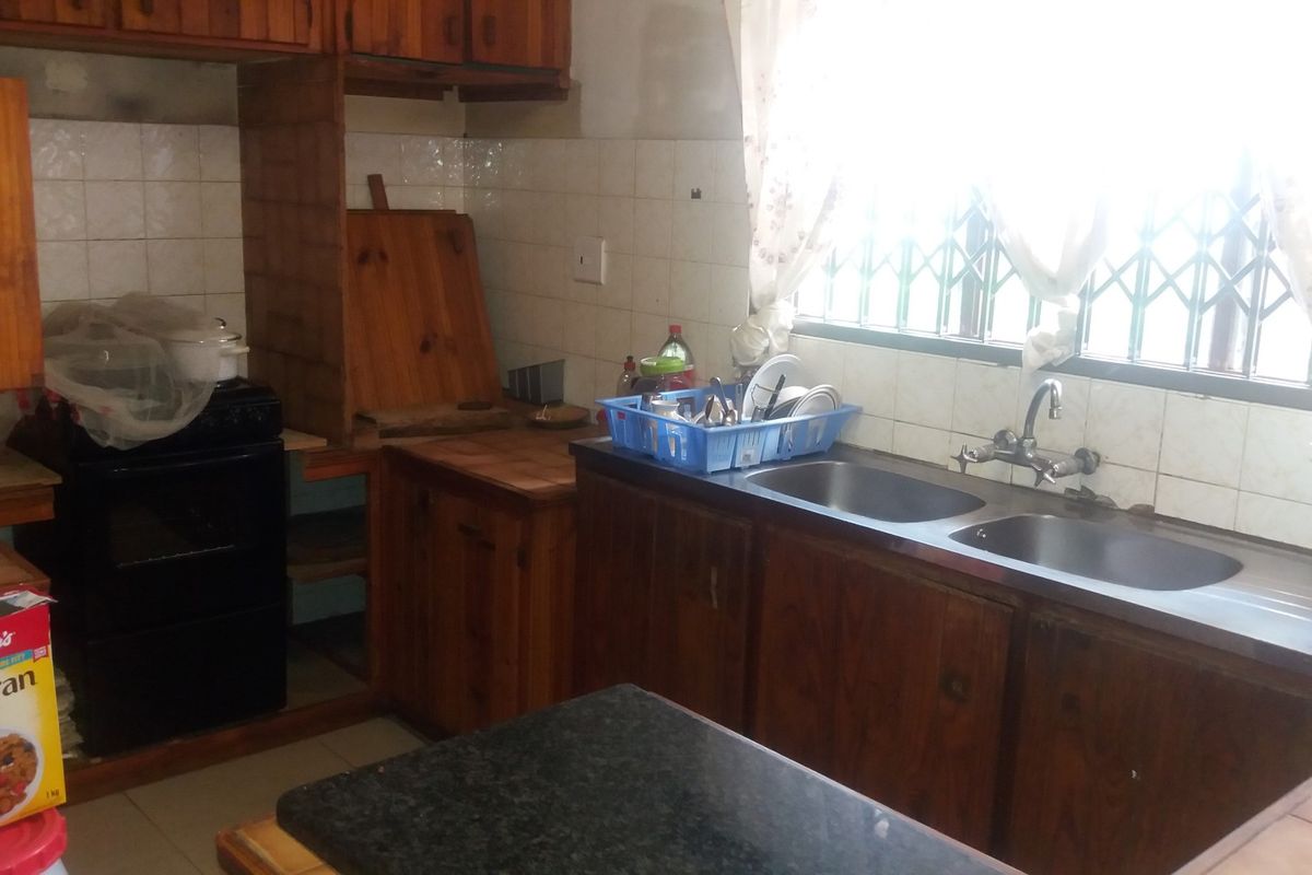 A dated kitchen featuring wooden cabinetry, a double bowl stainless steel sink, and tiled splashbacks, offering potential for a modern renovation.