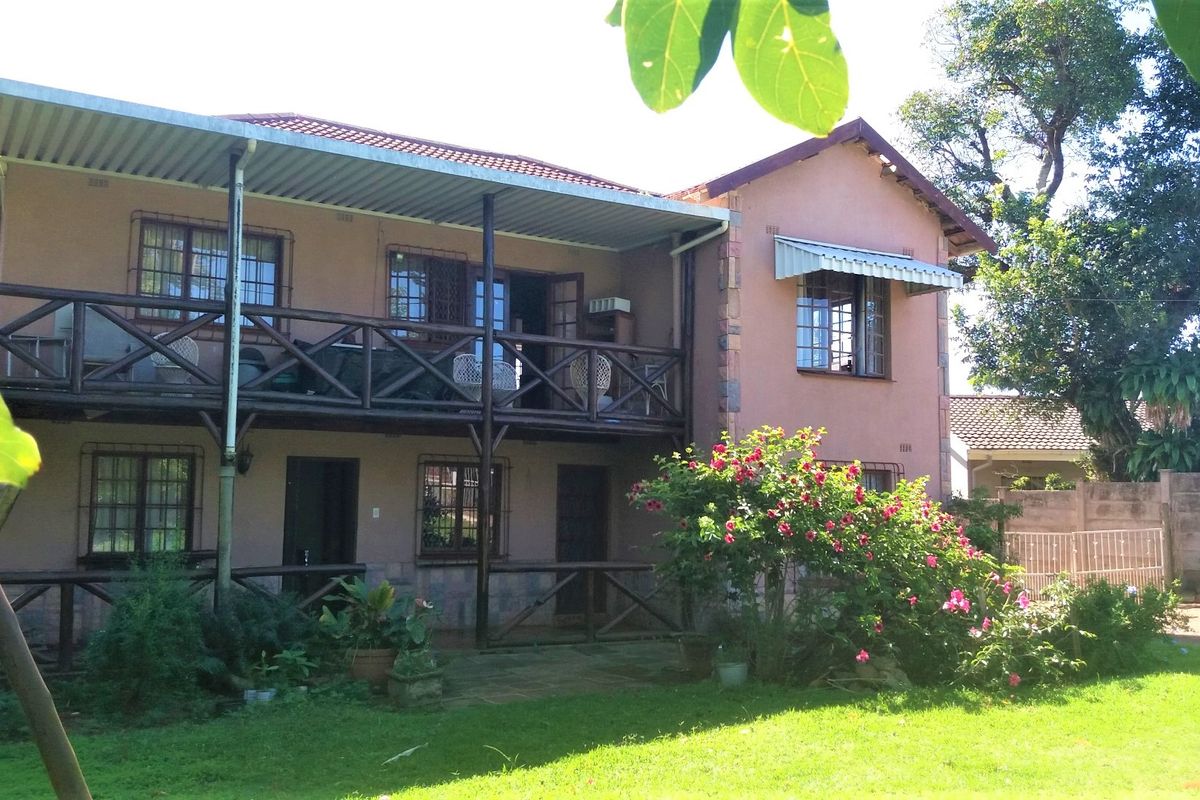 Rear view of a two-story house featuring a covered patio, upper-level balcony with timber balustrades, and a garden area.