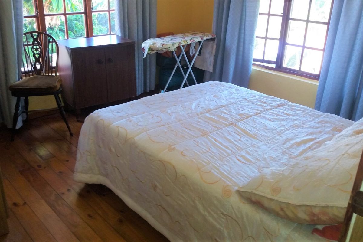 A bedroom featuring timber flooring and large timber-framed windows that provide natural light.