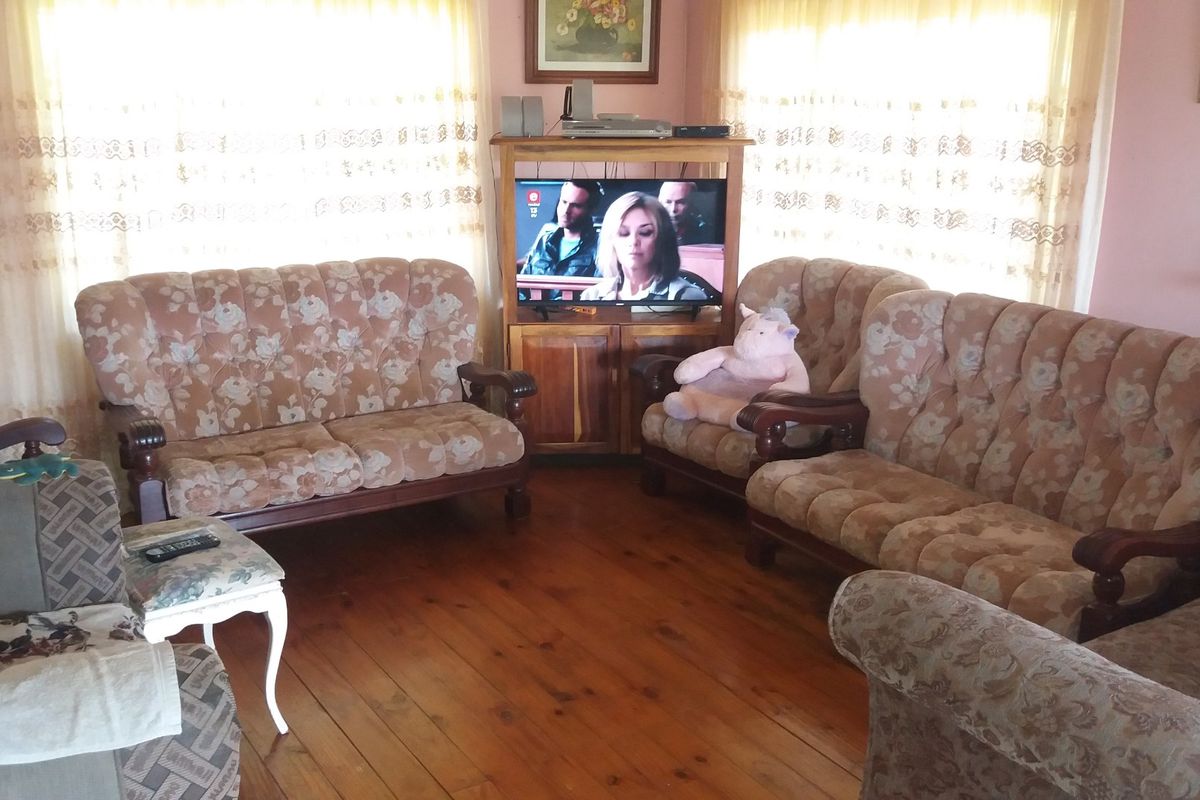 A traditional living room featuring warm timber flooring and large windows with curtains, offering a comfortable and classic living space.