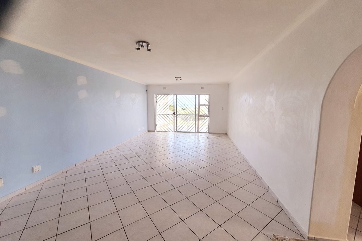 An empty, open-plan living area featuring ceramic floor tiles, a security gate, and an archway, currently undergoing wall surface preparation and painting.