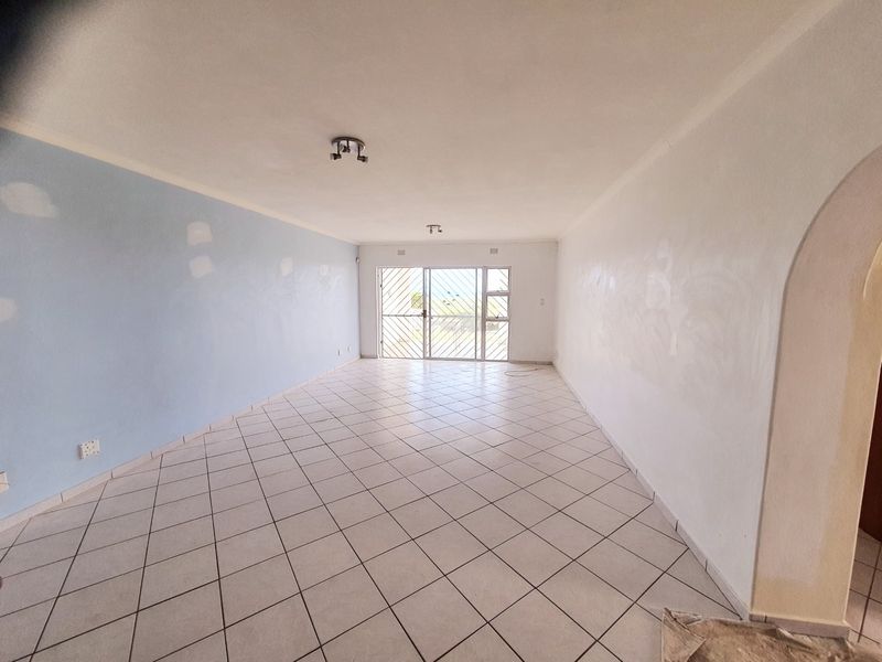 An empty, open-plan living area featuring ceramic floor tiles, a security gate, and an archway, currently undergoing wall surface preparation and painting.