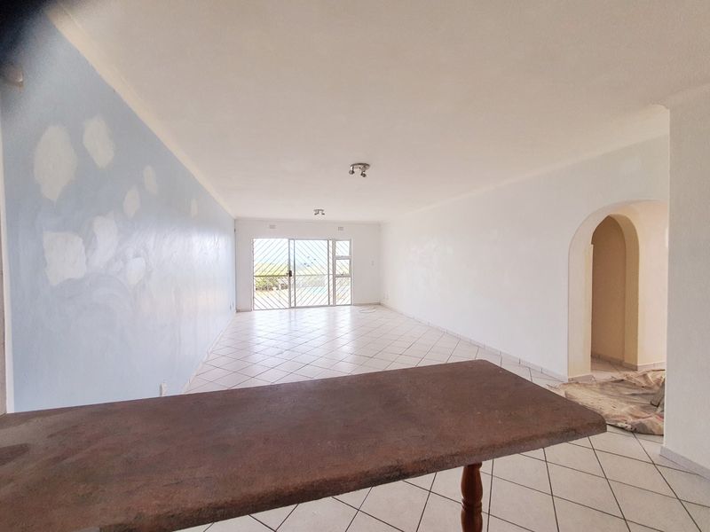 An empty open-plan living area featuring tiled floors, an arched entryway, and sliding doors leading to the exterior, currently undergoing wall painting.