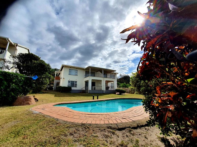 Exterior view of an apartment building featuring a swimming pool with brick coping and surrounding lawn area.