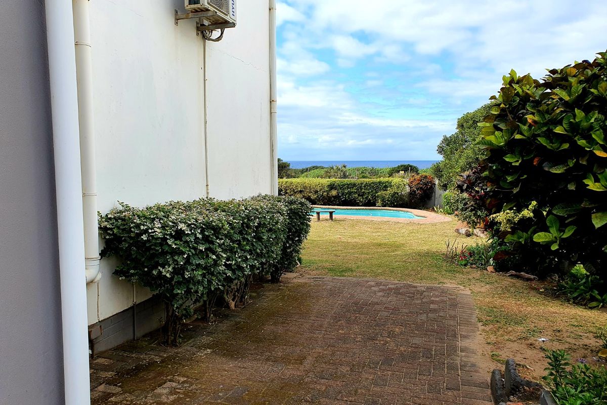 Rear exterior view featuring a paved patio, private swimming pool, and landscaped garden with distant ocean views.
