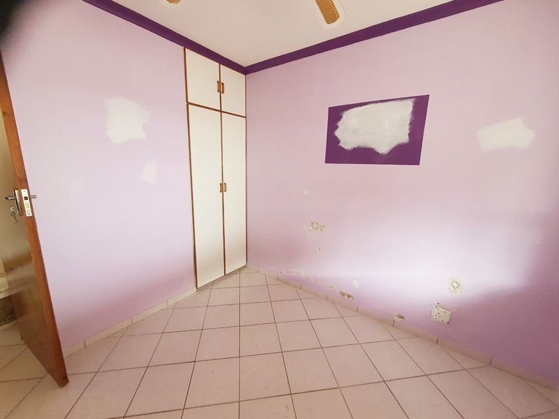 An empty bedroom featuring tiled flooring, a built-in cupboard, and a ceiling fan, currently requiring wall repairs and repainting.