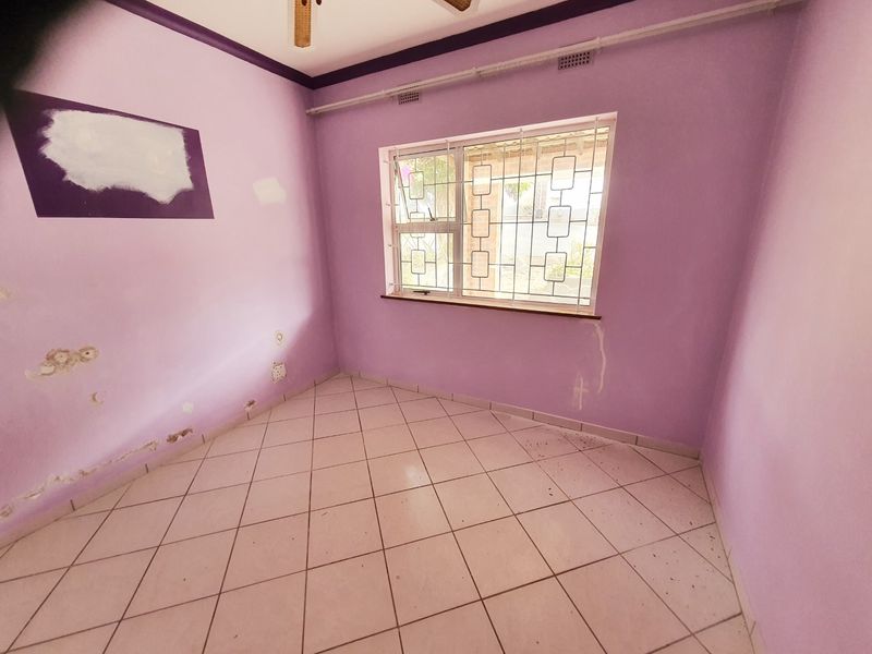 An empty bedroom featuring tiled flooring, security bars on the window, and a ceiling fan, requiring cosmetic wall repairs and repainting.
