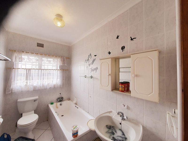 A dated bathroom featuring a standard bathtub, pedestal basin, and wall-mounted medicine cabinet with full-height wall tiling.