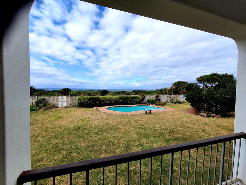 A view from a balcony overlooking a private garden with a swimming pool and distant ocean horizon.