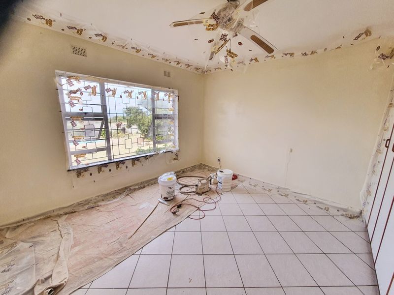 A bedroom currently undergoing renovation with tiled flooring, a ceiling fan, and security burglar bars on the window.