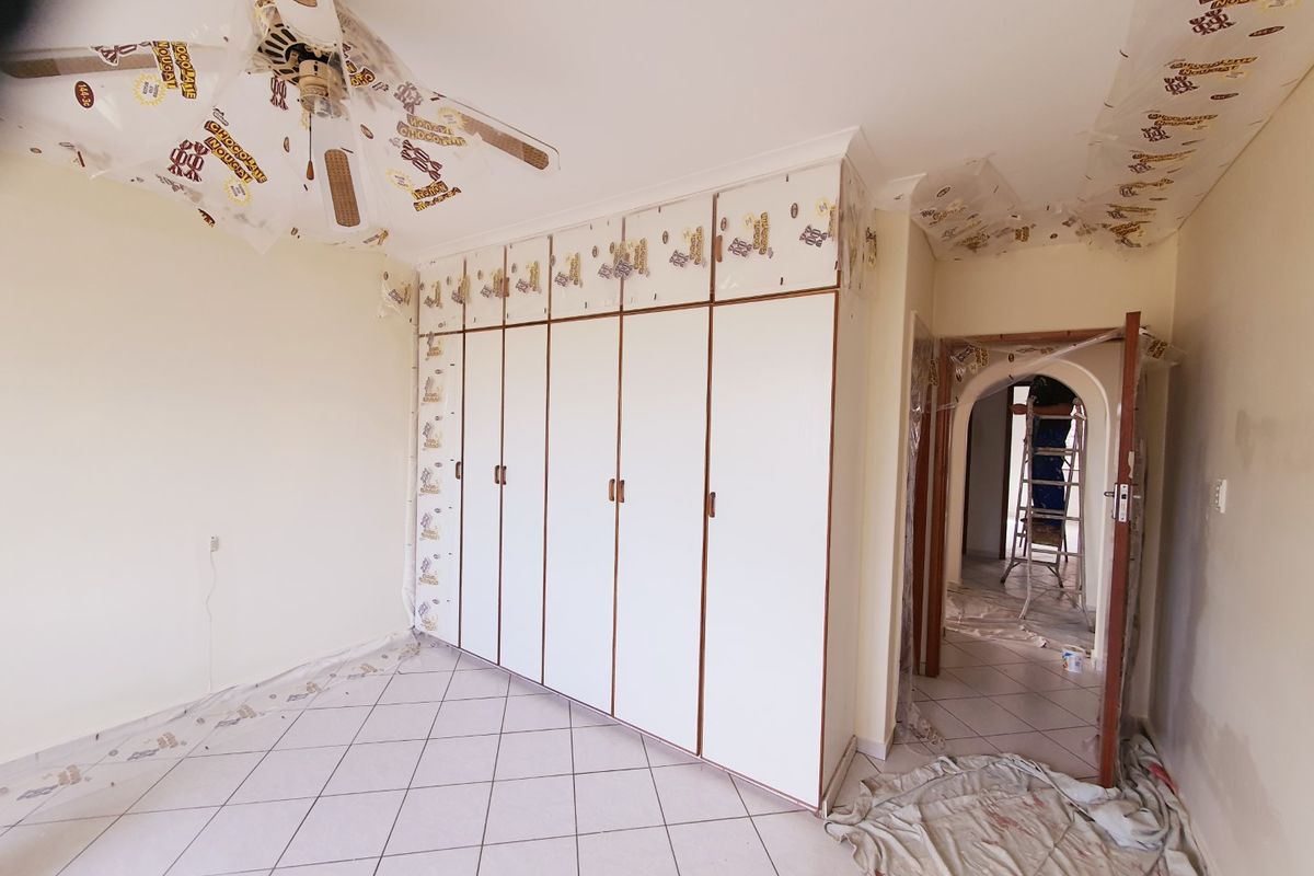 A bedroom currently undergoing renovations, featuring built-in cupboards, tiled flooring, and a ceiling fan, with protective plastic sheeting still in place.