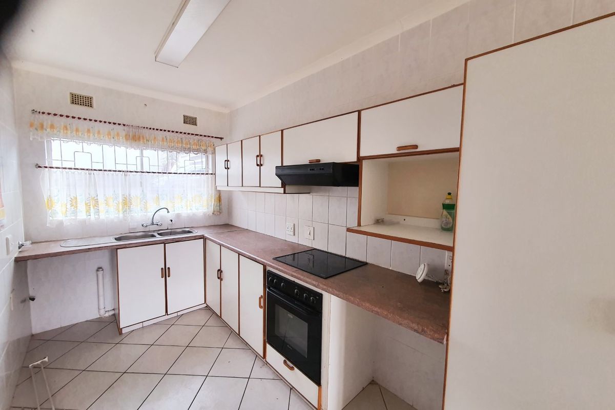A functional kitchen featuring built-in cabinetry, laminate countertops, a double basin sink, and integrated electric cooking appliances with tiled flooring and splashbacks.