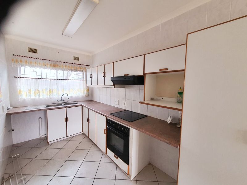 A functional kitchen featuring built-in cabinetry, laminate countertops, a double basin sink, and integrated electric cooking appliances with tiled flooring and splashbacks.