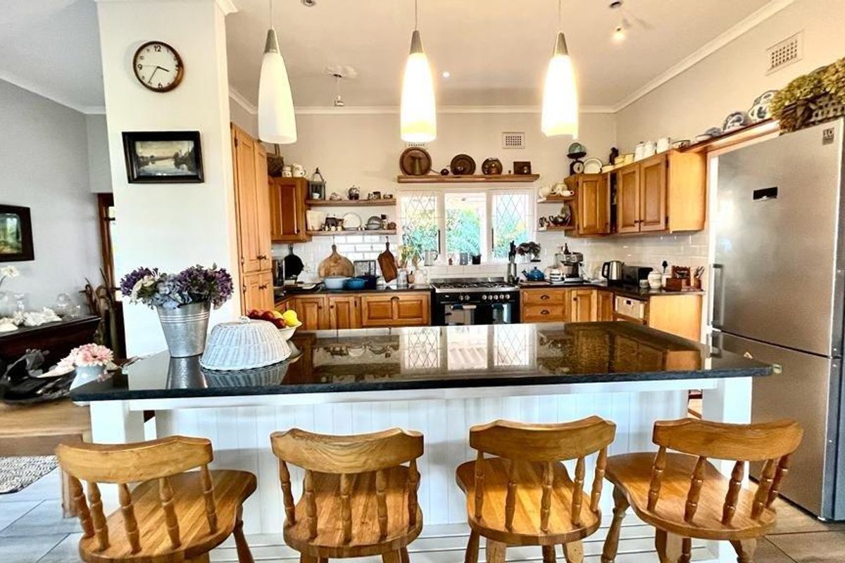 A traditional kitchen featuring wooden cabinetry, a central island with a dark stone countertop, subway tile backsplash, and integrated oven and hob.