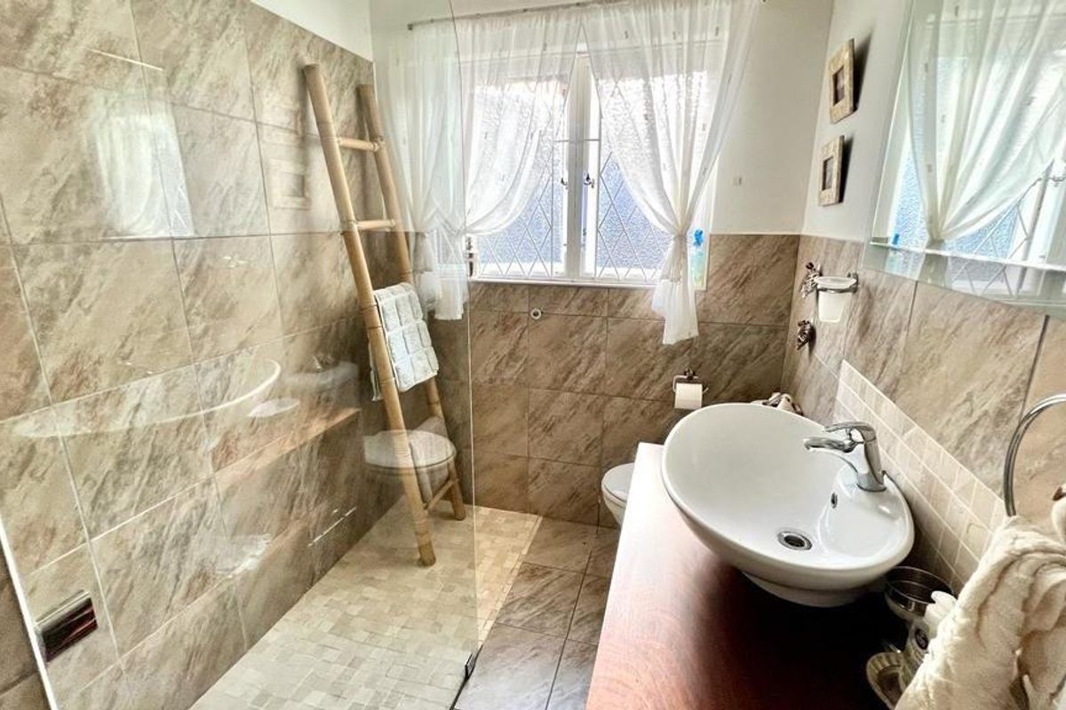 A functional bathroom featuring a walk-in shower with glass screen, tiled walls, and a modern vessel sink mounted on a wooden vanity unit.