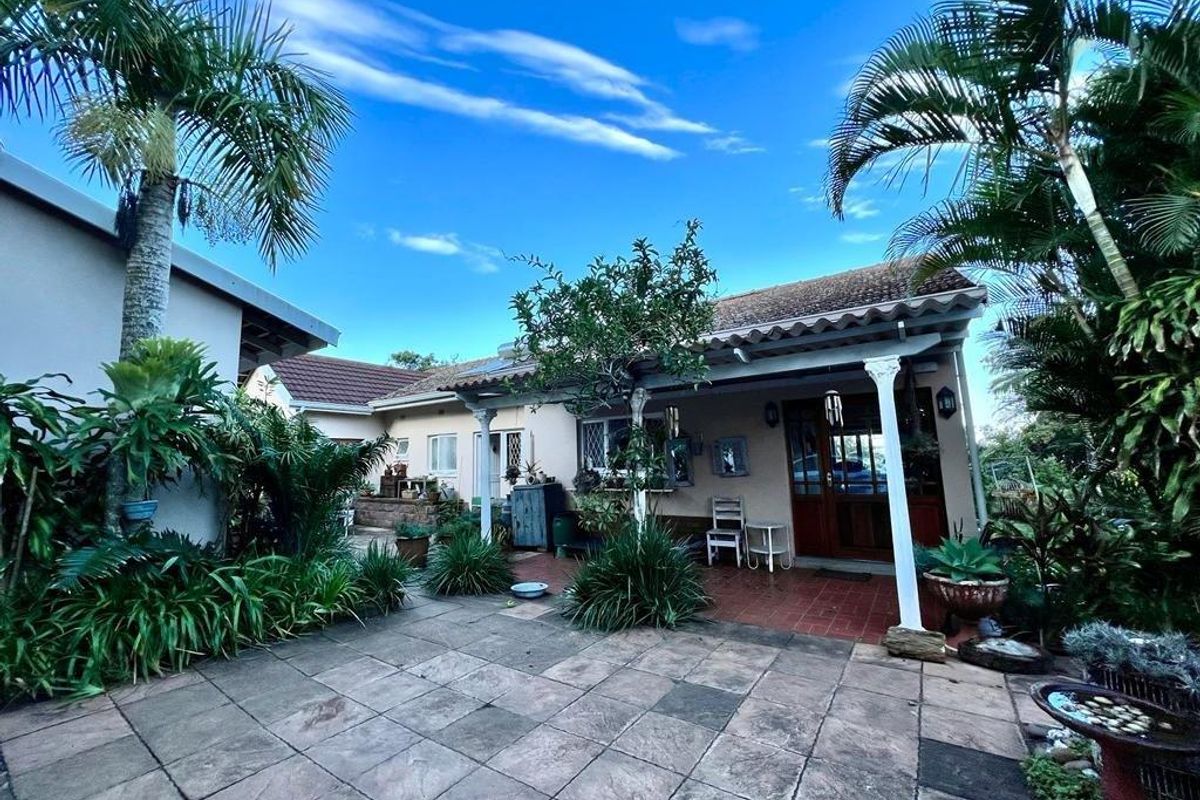A rear garden area featuring a paved patio, covered veranda with timber columns, and established tropical landscaping.