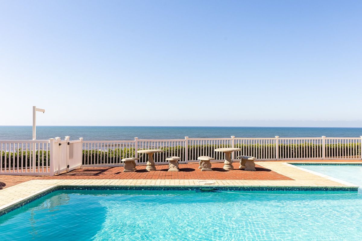 A well-maintained outdoor pool area featuring a brick-paved deck, white vinyl fencing, and expansive ocean views.