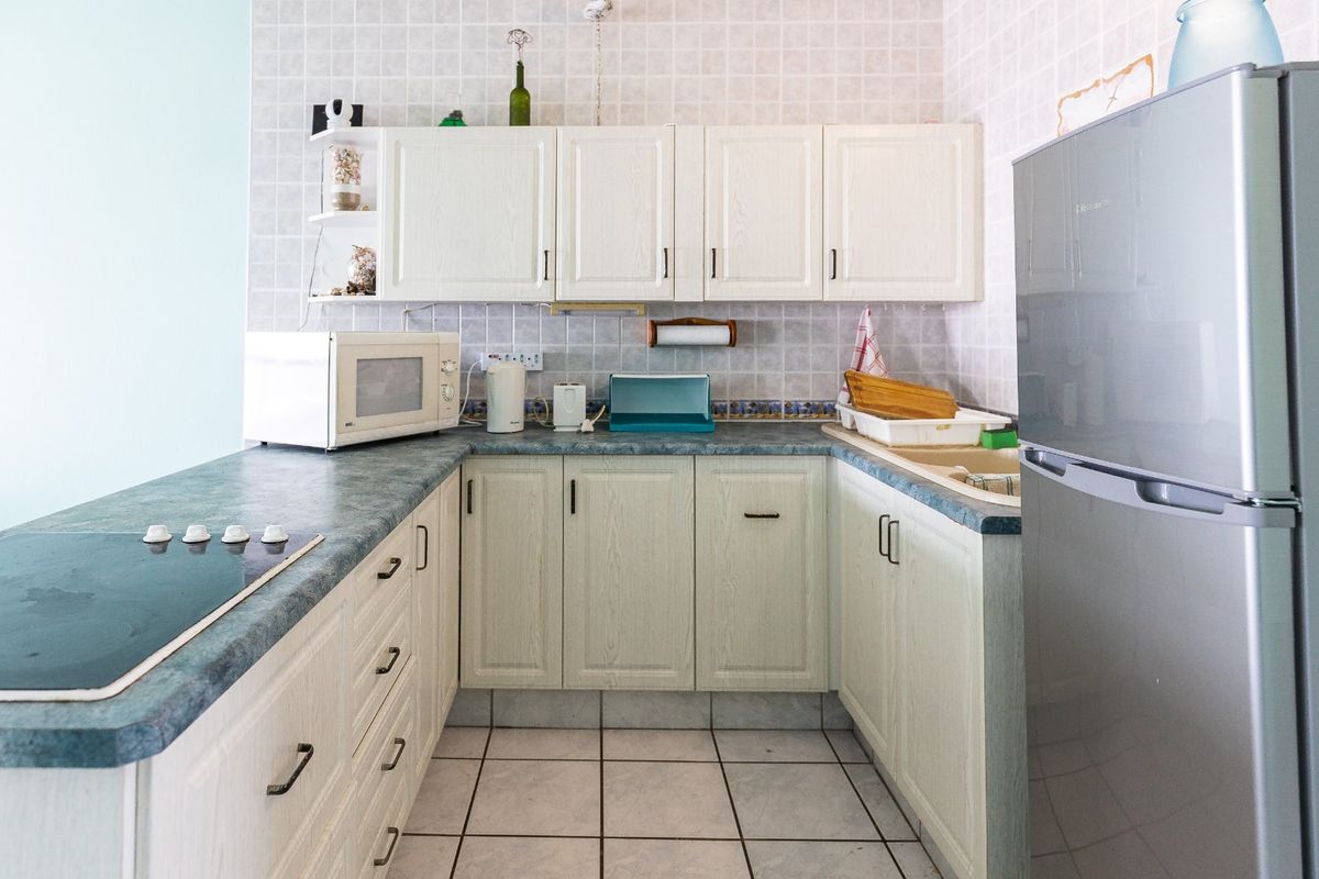 A functional U-shaped kitchen featuring white cabinetry, laminate countertops, a built-in electric hob, and tiled flooring.