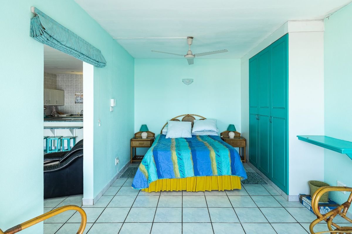 A bedroom featuring built-in teal cabinetry, tiled flooring, and a ceiling fan, with an adjacent view into the kitchen area.