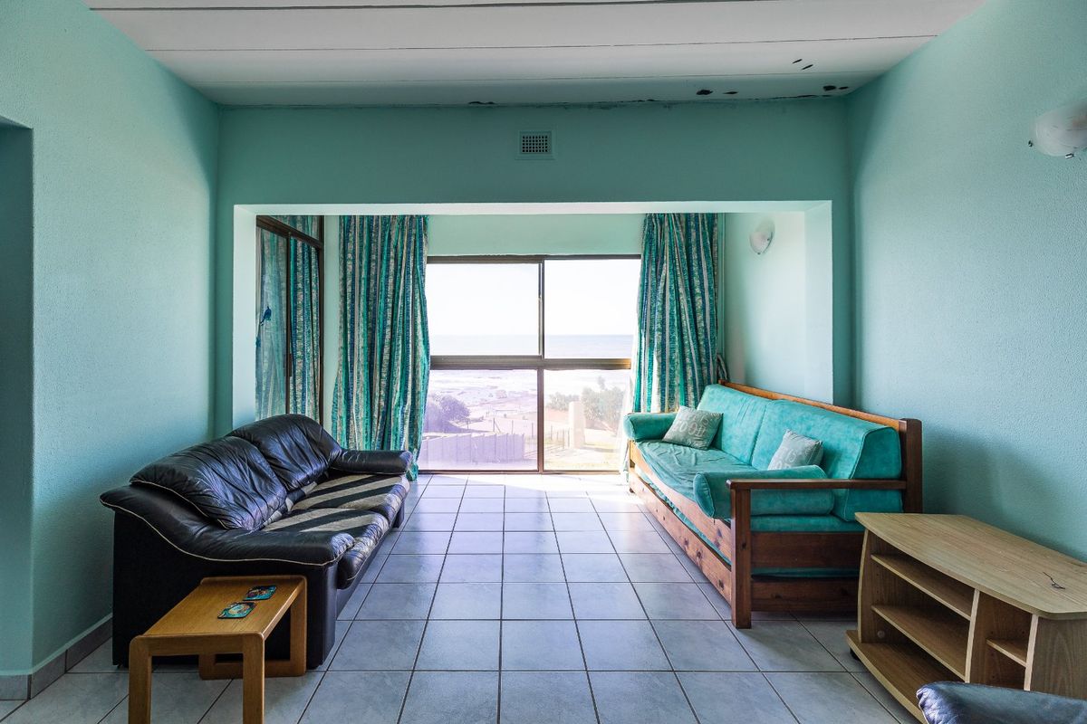 A living room featuring tiled flooring and large windows with ocean views, requiring some ceiling repairs and cosmetic updates.