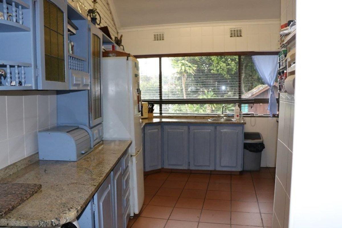 A functional kitchen featuring blue cabinetry, granite countertops, tiled flooring, and a large window overlooking the garden.