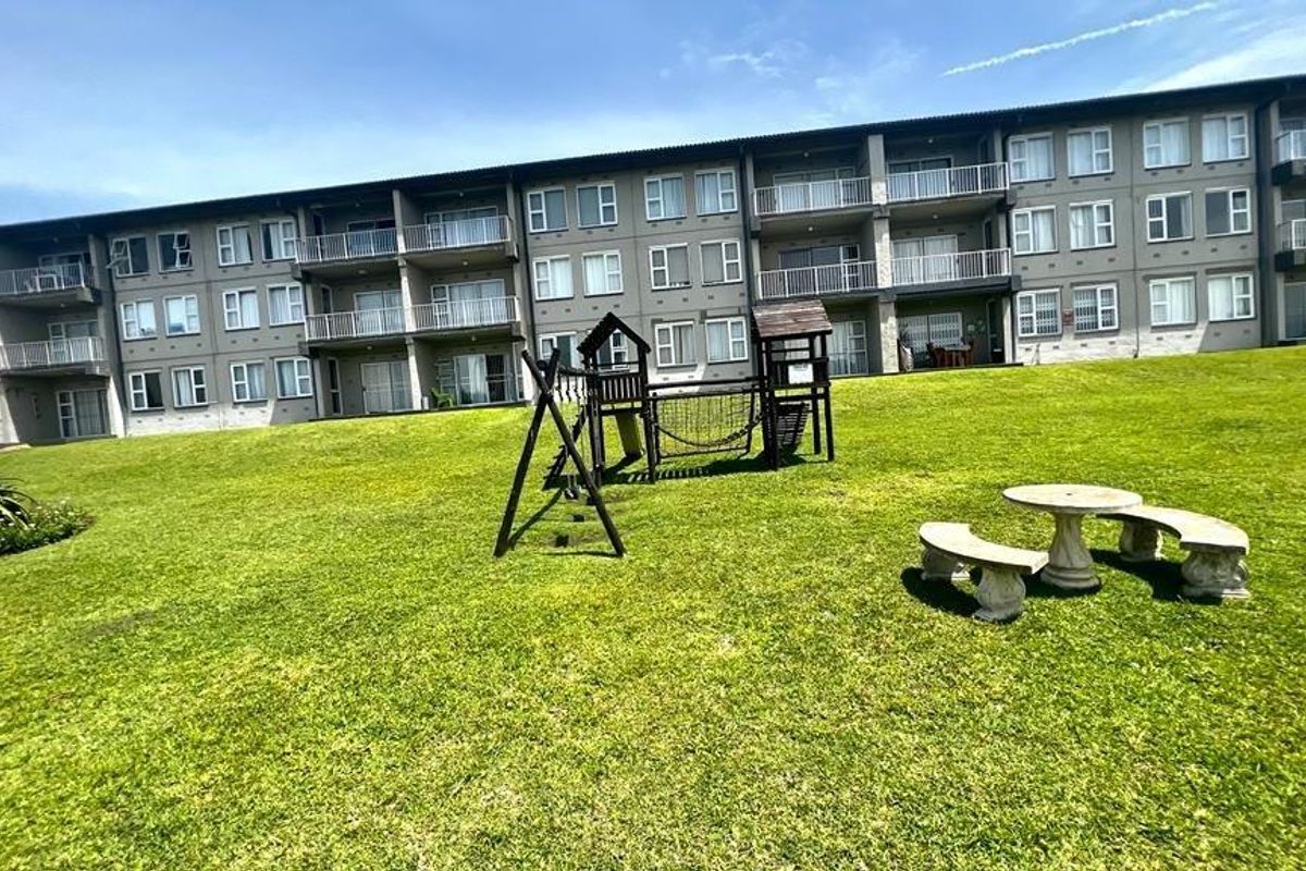 Rear view of a multi-story apartment complex featuring private balconies and a shared communal garden area with playground equipment.