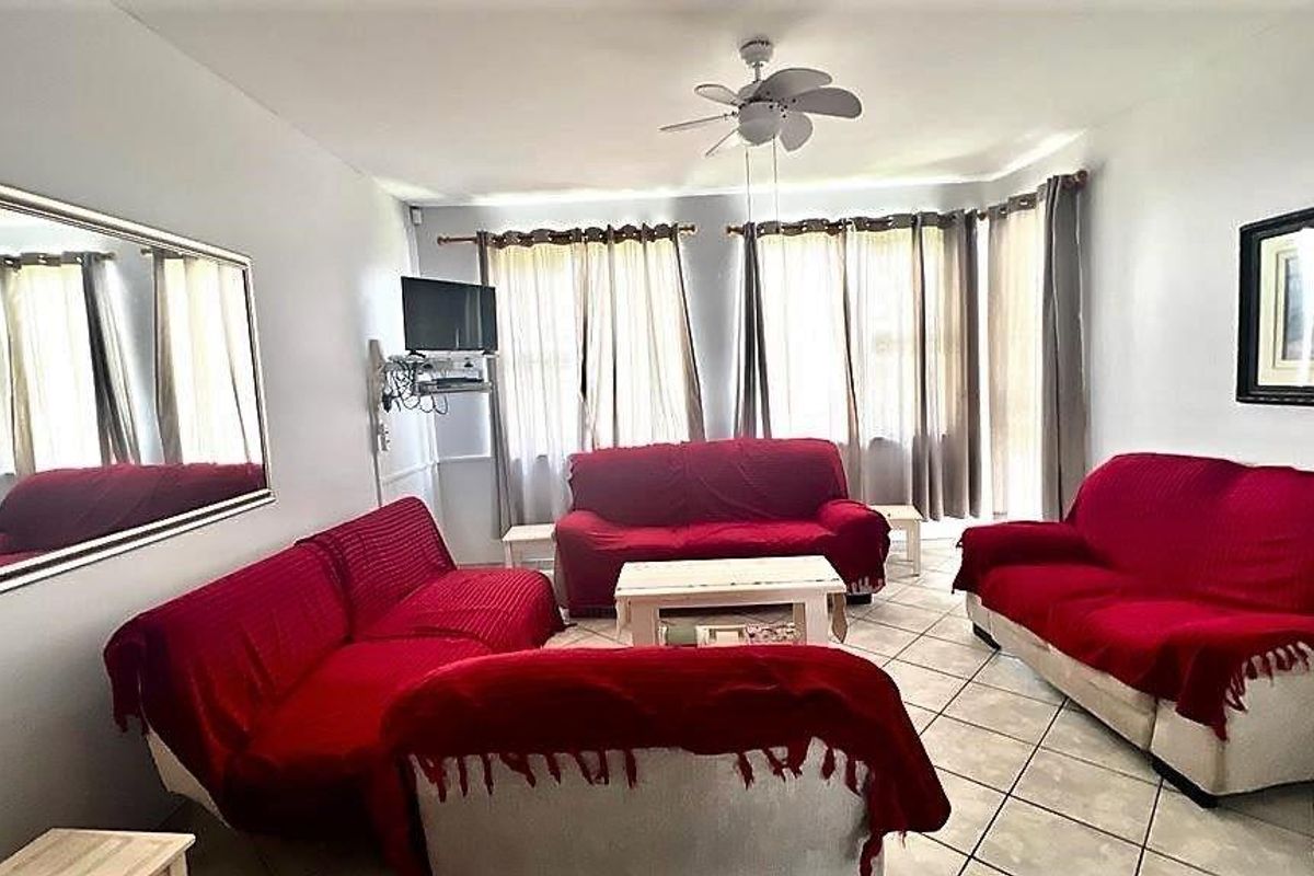A living room featuring tiled flooring and a ceiling fan, with large windows allowing natural light into the space.