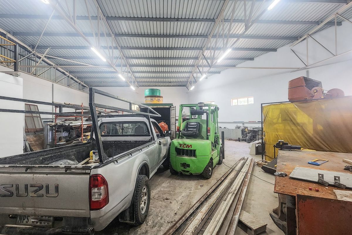 Spacious industrial utility area featuring high ceilings with exposed steel trusses, fluorescent lighting, and durable concrete flooring, suitable for workshop or storage operations.